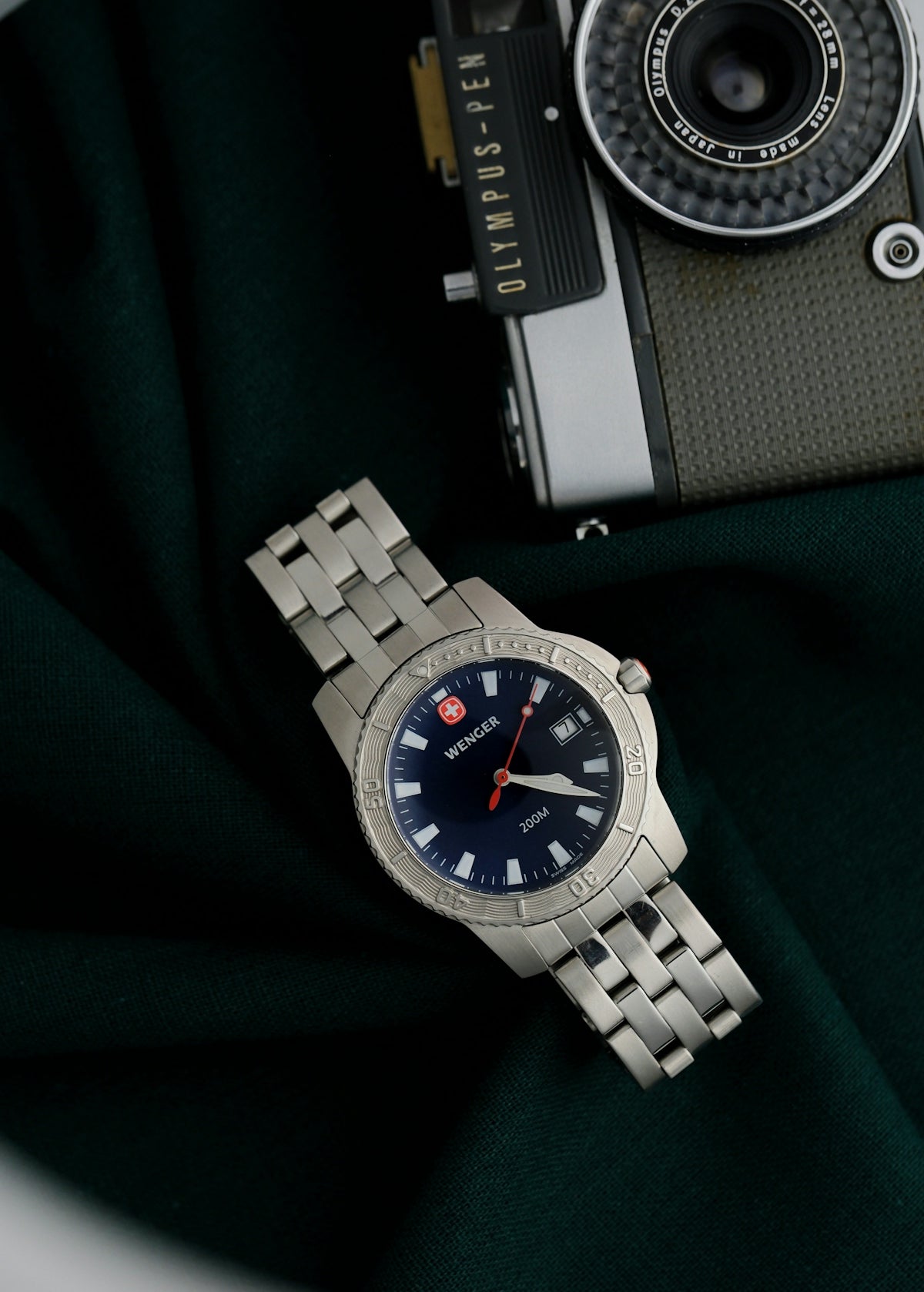 A stainless steel watch rests on a dark green cloth.