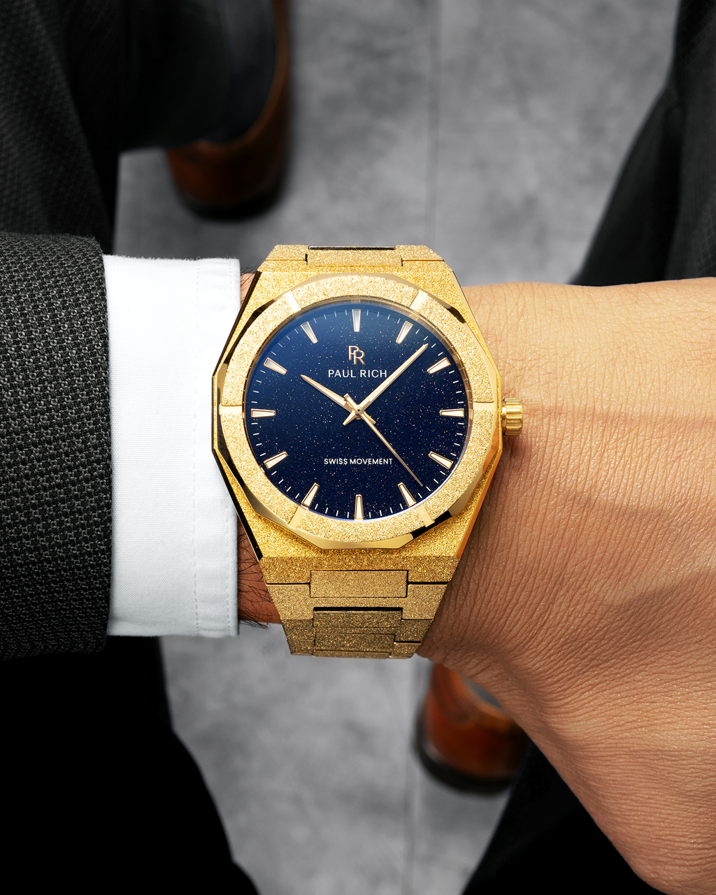 Gold watch with blue dial on a wrist, worn by a person in formal attire.