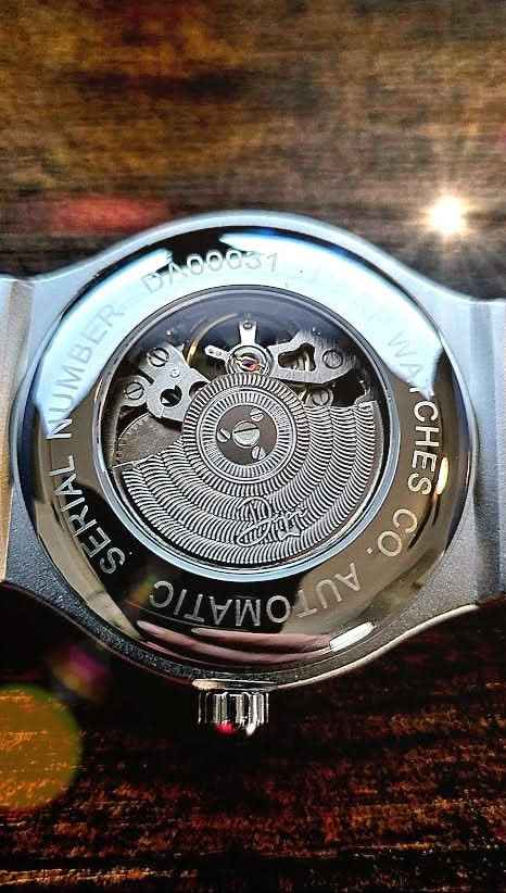 Silver-toned automatic watch with a visible mechanical movement and engraved text around the case back.